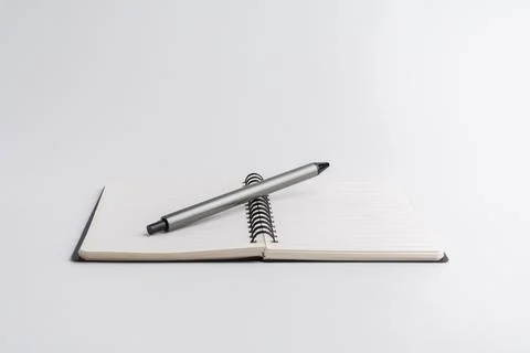 Blank open notebook with a grey pen resting on its pages isolated on white .. Stock Photos