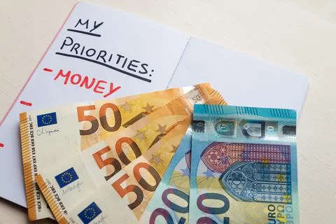 Blank page of diary, with text "Priorities", "Money", and banknotes beside it. Stock Photos