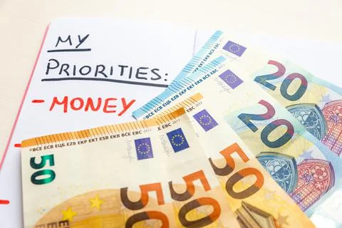 Blank page of diary, with text "Priorities", "Money", and banknotes beside it. Stock Photos