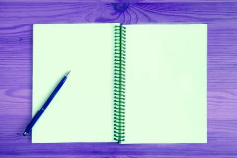 Blank page of an opened notebook with a blue pen on purple wooden table Photos