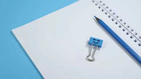 Blank Paper Notepad with Blue Pencils and Smile Binder Clip on Blue Background Stock Footage 136965607