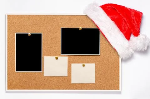 Blank paper notes and an empty photo are pinned to a cork board. Santas hat on a Stock Photos