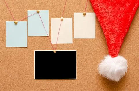 Blank paper notes and an empty photo are pinned to a cork board. Santa's hat  Stock Photos