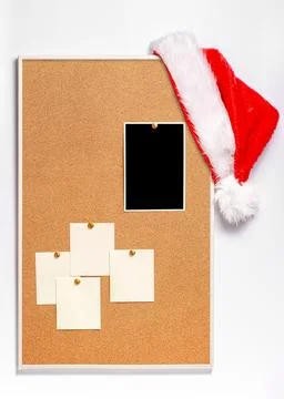 Blank paper notes and an empty photo are pinned to a cork board. Santa's hat  Stock Photos