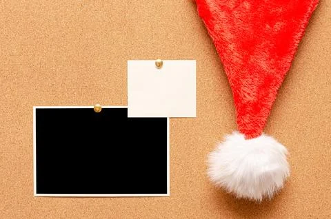 Blank paper notes and an empty photo are pinned to a cork board. Santa's hat  Stock Photos