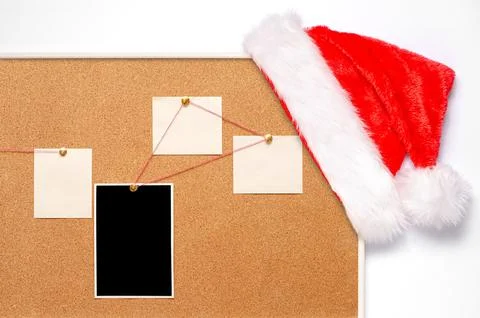 Blank paper notes and an empty photo are pinned to a cork board. Santa's hat  Stock Photos