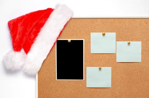 Blank paper notes and an empty photo are pinned to a cork board. Santas hat on a Foto stock