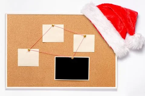 Blank paper notes and an empty photo are pinned to a cork board. Santa's ha.. Stock Photos