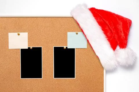 Blank paper notes and an empty photo are pinned to a cork board. Santa's hat  Foto stock