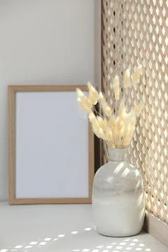 Blank photo frame and vase with dried plant on white window sill Stock Photos