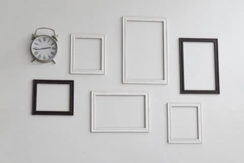 Blank picture frames and clock on white cement wall. Stock Photos