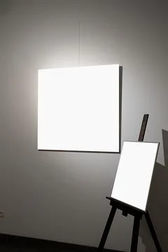 Blank picture frames on grey wall with glowing lamp, mock up Stock Photos