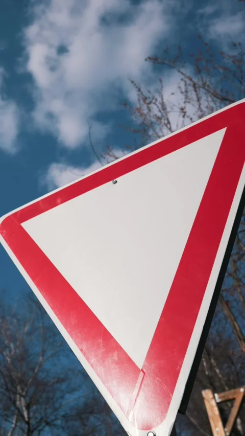 Blank red and white triangular road warning sign against a blue cloudy sky. 스톡 동영상 331861631