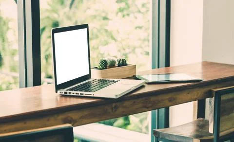 Blank screen laptop computer and tablet on wood stool table near window at ca Stock Photos
