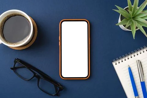 Blank screen smartphone on blue table. Coffee cup, notepad, pen and glasses.. Stock Photos