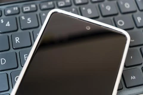 Blank screen on a smartphone lying on a black laptop keyboard. view from above Stock-Fotos