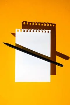A blank sheet of Notepad, black pencil and hard shadows on bright yellow back 写真素材