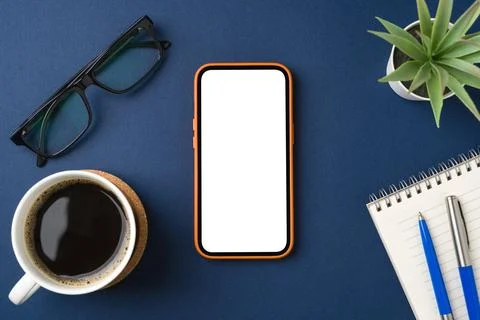 Blank smartphone on blue table. Coffee cup, notepad, pen and glasses around Stock Photos