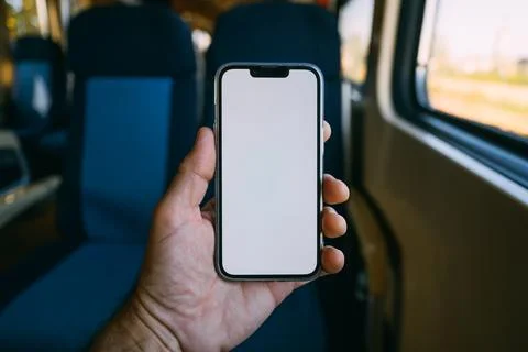 Blank smartphone screen held in front of passenger seats inside a train. Mo.. Fotos Stock