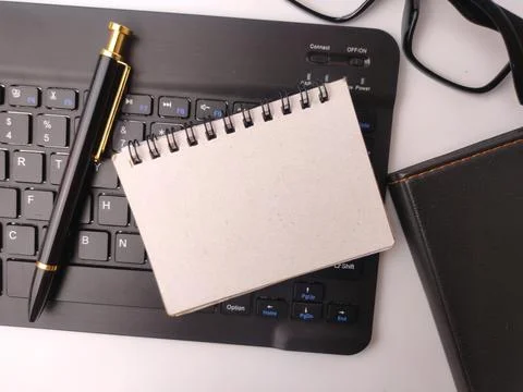 A blank spiral notepad, a black elegant pen, glasses, and a closed leather .. Stock Photos