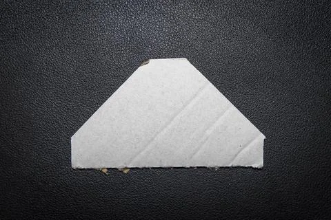 A blank, triangular piece of white paper placed on a textured black surface, Fotos de archivo