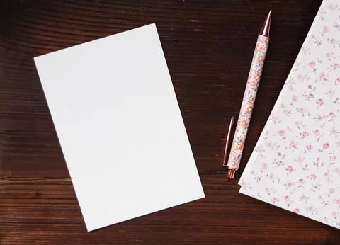 Blank white card, floral pattern notebook, and pen on a dark wooden backgro.. Stock Photos