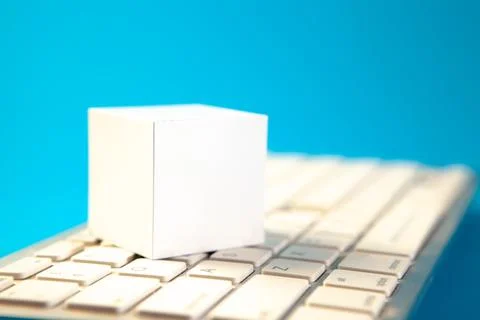 Blank white paper cube on computer keyboard isolated on blue background. Stock Photos
