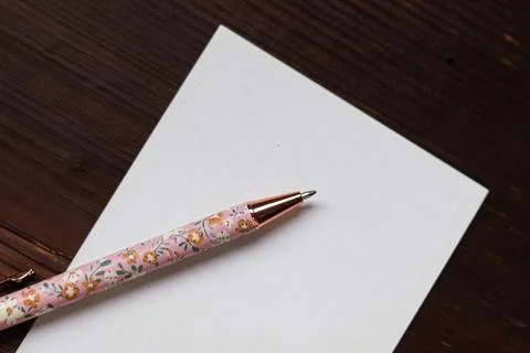 Blank white paper with a floral patterned pen on a dark wooden desk, ready .. Stock Photos