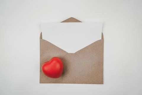 Blank white paper is placed on the open brown paper envelope with red heart. Stock Photos