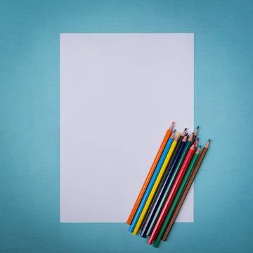 A blank white sheet and colored pencils for drawing on a plain textured backg Stock Photos
