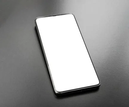 Blank white smartphone screen mockup standing upright on a dark metallic ta.. Stock Photos