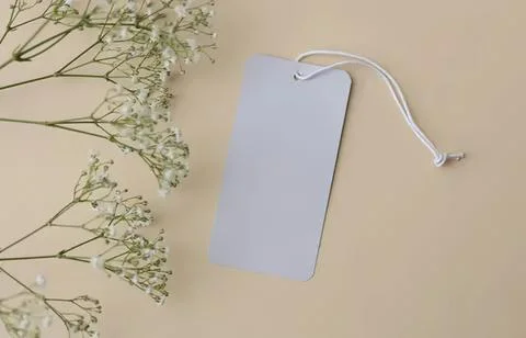 Blank white tag with string lying on beige surface Stock Photos