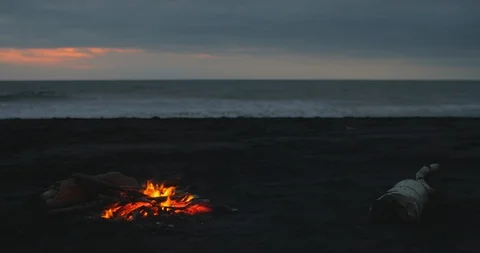 Blazing campfire with bright flames on the black sand beach at sunset. Stock Footage 123398792