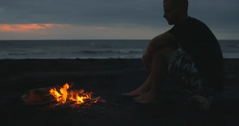 Blazing campfire with bright flames on the black sand beach at sunset. Stock Footage 123399480