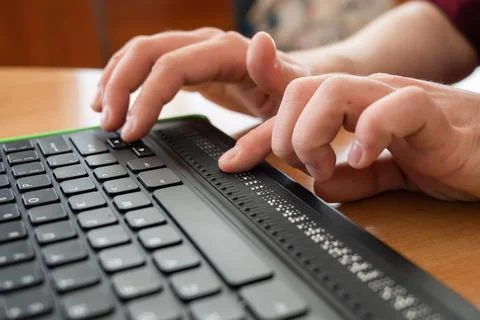 A blind man uses a computer with a Braille display and a computer keyboard Stock Photos