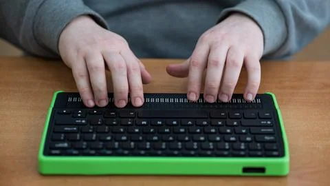 A blind man uses a computer with a Braille display and a computer keyboard 写真素材