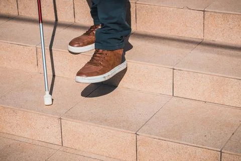 A blind person tries to go down the stairs helping himself with a cane, Foto stock