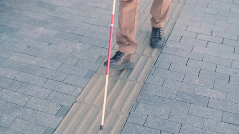 Blind person using white cane on straight tactile tiles to navigate road Stock Footage 221368562