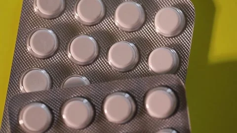 Blister with white flat tablets slowly rotating on yellow background Stock Footage 306074265