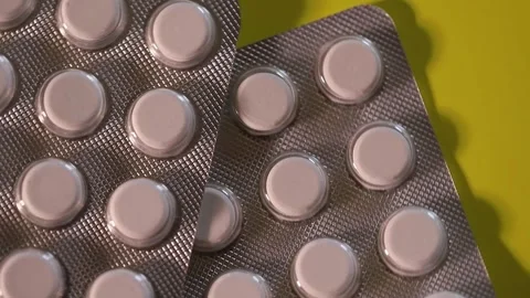 Blister with white flat tablets slowly rotating on yellow background Stock Footage 306074281