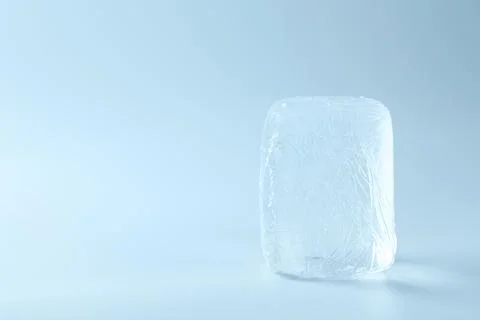 Block of clear ice on light blue background, space for text Stock Photos