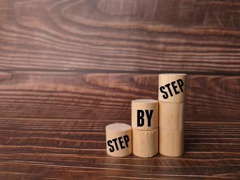 Block cylinder with text STEP BY STEP on a wooden background. 写真素材