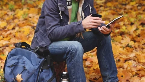 Blogger in forest, drinks and working tablet computer, looking map,  autumn hike Video stock 103562355