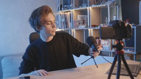 The blogger guy sits down at the table,puts the microphone in,greets the camera. Vidéo 204074763