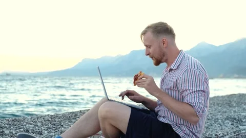 Blogger talking on laptop while sitting on the beach 스톡 동영상 220863011
