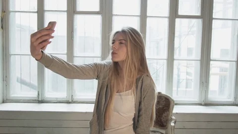 A blond blonde on the opposite window makes selfie using a smartphone. Beautiful Stock Footage 75003000