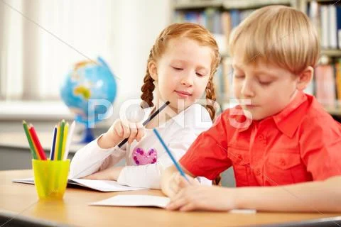 A blond boy and a red haired girl sitting at table and drawing Stock Photos