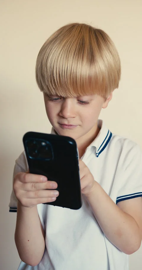 A blond boy with blue eyes is using a phone, trying to type a message and 스톡 동영상 323116590