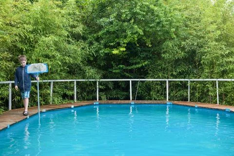 A blond boy in a blue jacket with a net by the pool Stock Photos