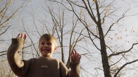A blond boy cheerfully throws up fallen leaves. Stock Footage 262759866